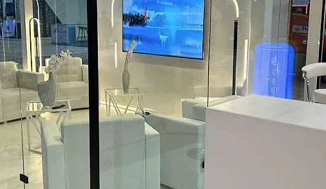 جناح IT Belt Company (ITB): غرفة اجتماعات بجدران زجاجية وأرائك بيضاء وشاشة جدارية وعمود عرض مضاء