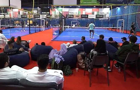 متفرجون على أكياس جلوس ومقاعد استراحة فوق أرضية حمراء بجوار ملاعب البادل في Padel In KSA