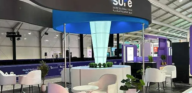 جناح SurePay: مظلة دائرية زرقاء فوق عمود زجاجي مضاء، ومكتب جزيرة مزروع، ومقاعد استراحة بيضاء