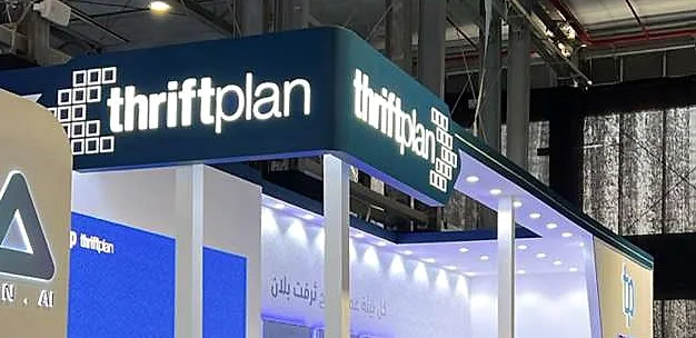 جناح thriftplan: واجهة علوية كحلية مضاءة تحمل شعار thriftplan فوق جدران بيضاء ورسومات زرقاء