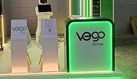 جناح Vego Group: مكتب أبيض تحيط به إضاءة خضراء، وحوامل عرض، وروبوت خدمة